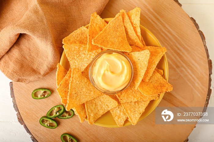 Plate with tasty nachos and sauce on light background