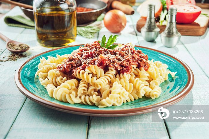 Fusilli pasta with bolognese meat sauce on a coloured plate