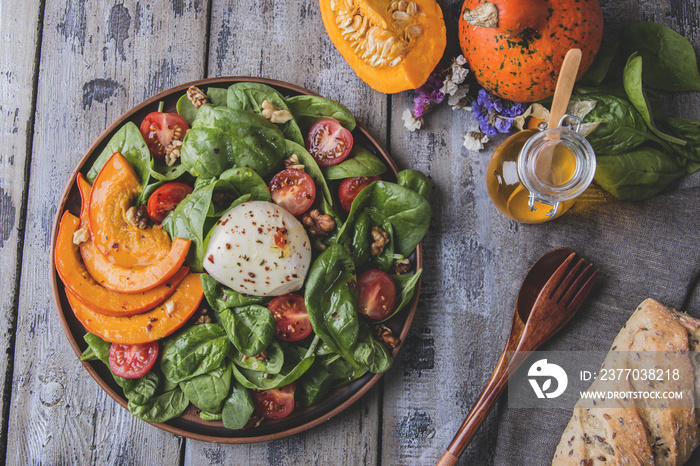 salad with baked pumpkin, mozzarella cheese, spinach greens, tomatoes in a plate on a wooden table