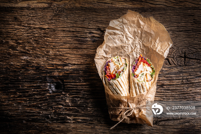 Grilled tortilla wraps with chicken and veggies wrapped in a paper, placed on a rustic wood