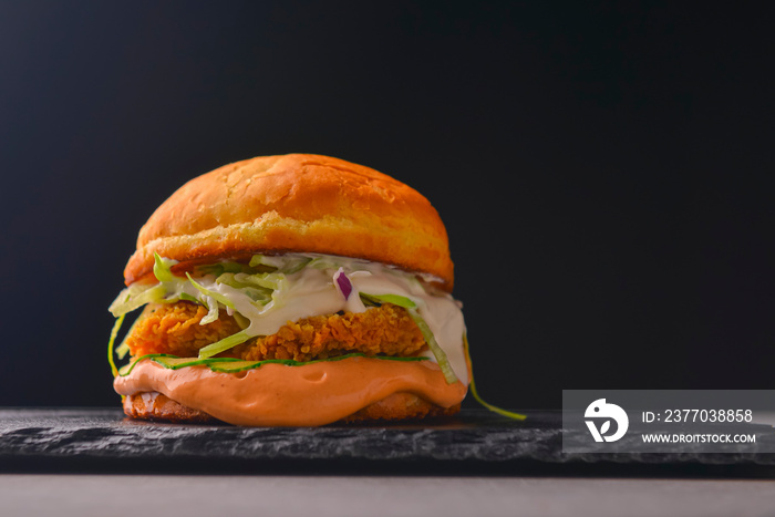 Juicy delicious craft burger with spices on a black background. Fast food, junk food concept.