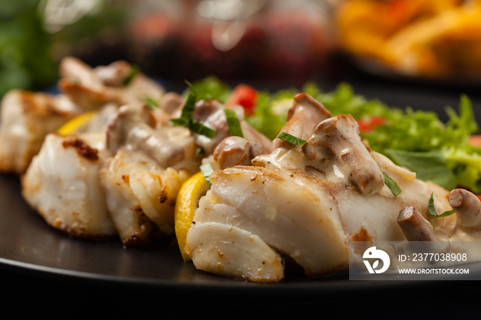 Fried cod served with mushroom sauce and salads. Portion on a black plate. Dark background.