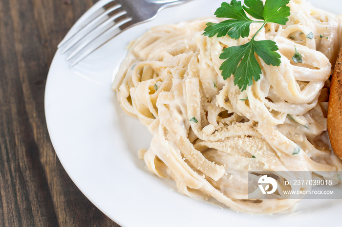 Plate of fettucini alfredo with fresh parsley and a slice of french bread. Top view.