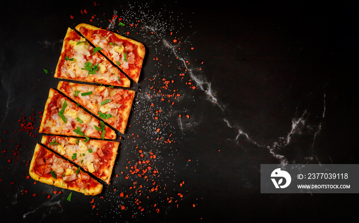 Sliced Hawaiian pizza on black stone background, top view.