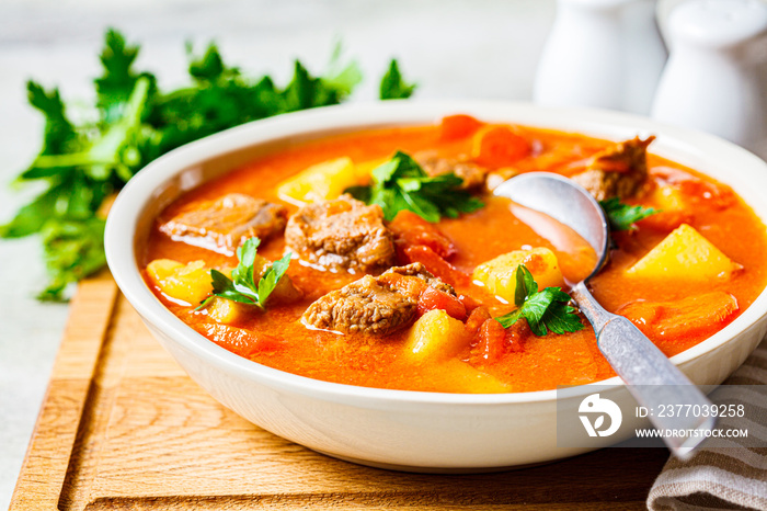 Soup with beef and vegetables in white plate on a wooden board. Traditional meat shurpa soup with vegetables and herbs.