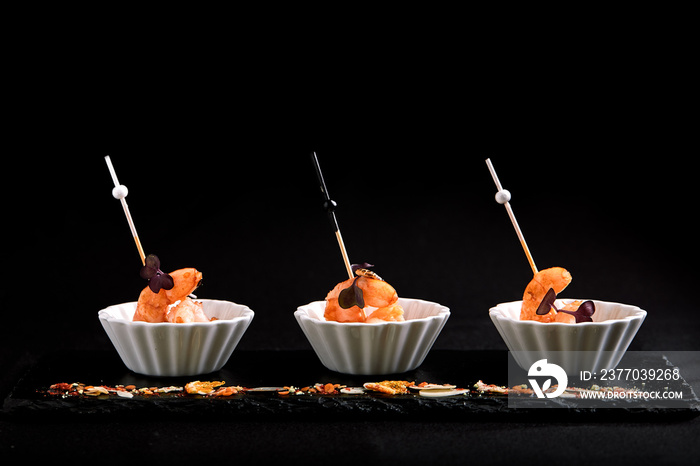 Canapes with tiger prawns on a skewer on a black background. The concept of catering food.