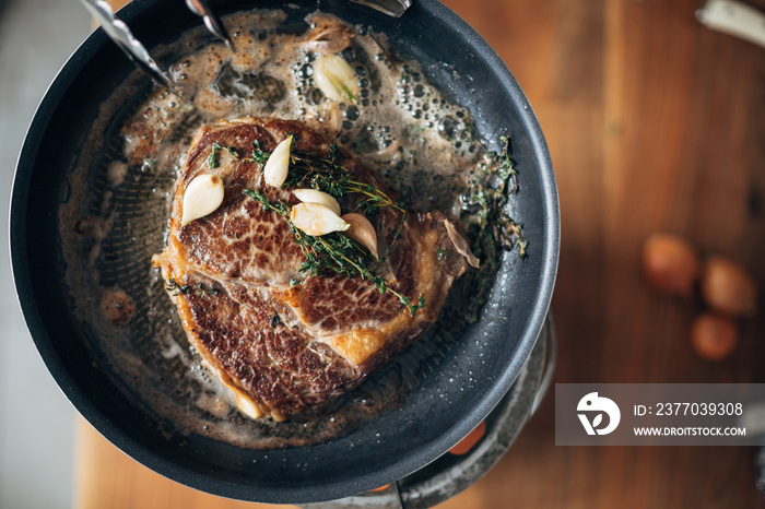 Overhead shot of chef preparing ribeye with butter, thyme and garlic. Keto diet.