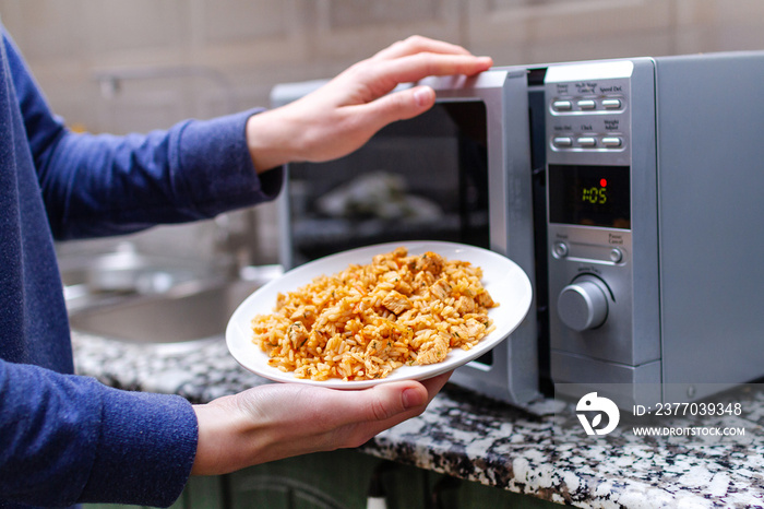 Using a microwave to warming a plate of homemade pilaf for lunch at home. Hot meal