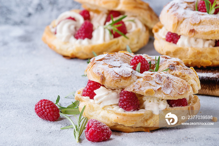 Homemade choux pastry cake Paris Brest with raspberries, almond, sugar powder and rosemary, served over gray blue texture background. Close up. French dessert