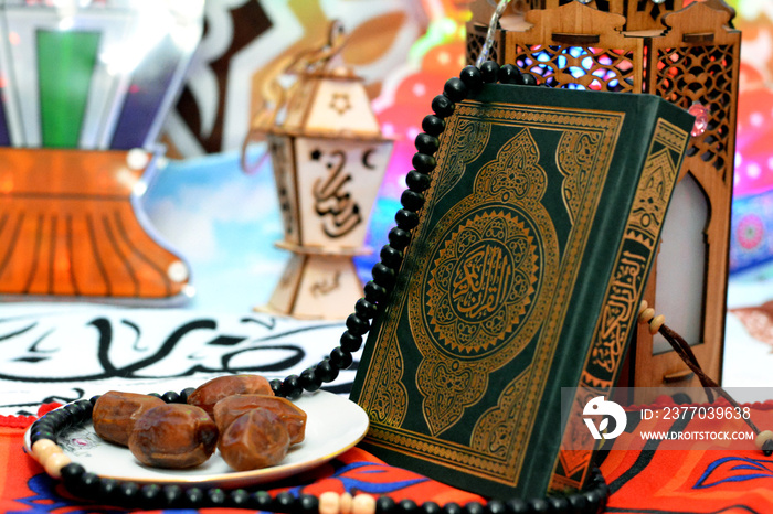 Selective focus of Islamic Ramadan month colorful background, A holy Quran with Islamic rosary, dates fruit on a white plate and blurred Ramadan lanterns fanous, Translation of Arabic Text (Ramadan)