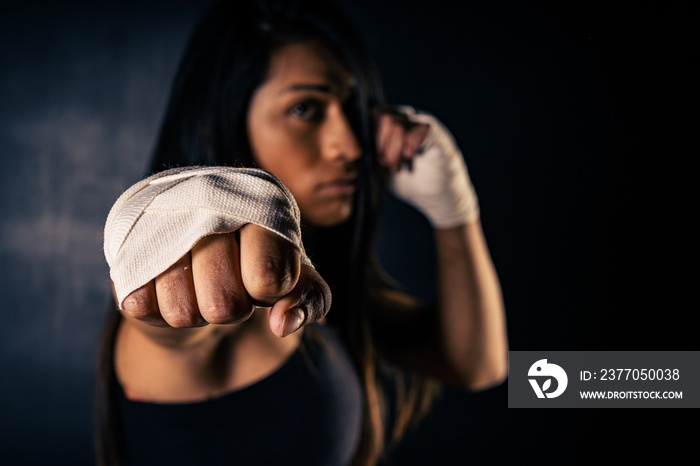 Young latin woman practicing boxing and kickboxing. She scores a direct punch with her fist. Differential focus. Sport, fitness, training concept.