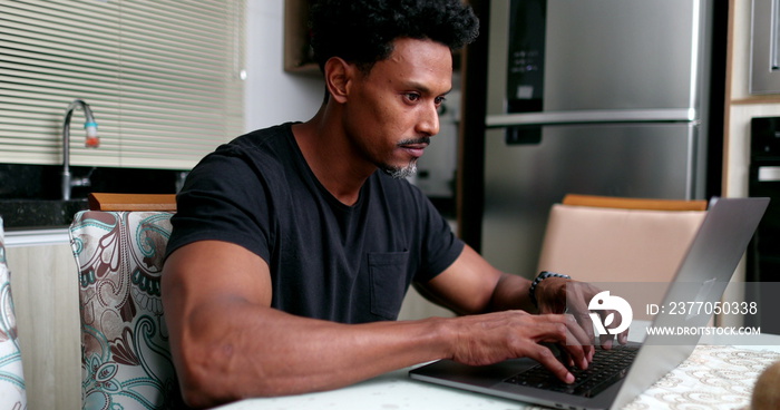 African man working from home sitting at kitchen table using laptop