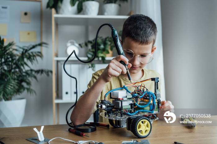 Cute child in casual clothes assemble robot. Kid constructs metal robot and program it. The boards and microcontrollers are on the table. STEM education inscription, programming, mathematics