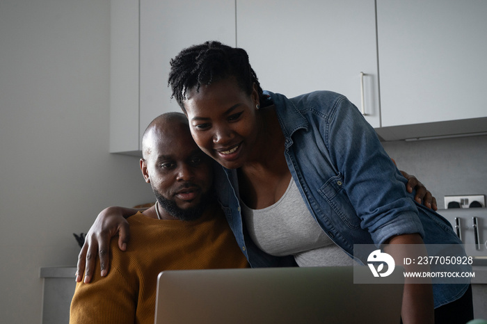 Man and pregnant woman looking at laptop in kitchen