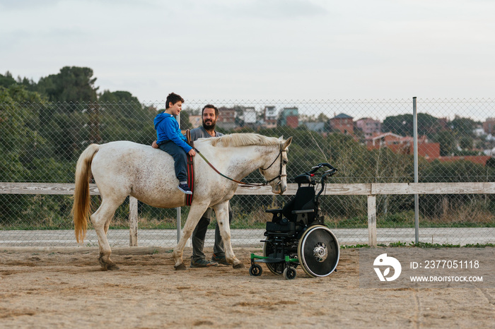 Boy with disabilities riding a horse while having an equine therapy session with an instructor.