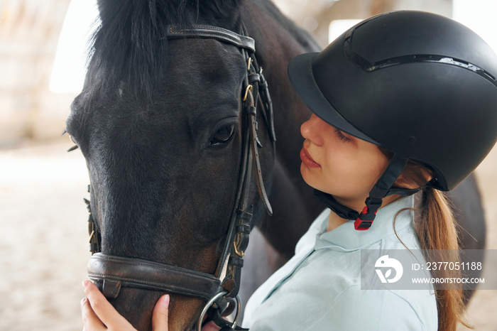 Close up view. A young woman in jockey clothes is preparing for a ride with a horse on a stable