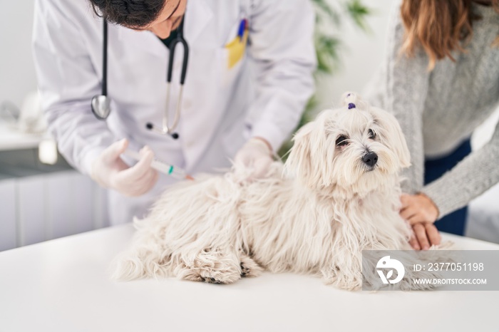 Man and woman veterinarian vaccinating dog at veterinary clinic