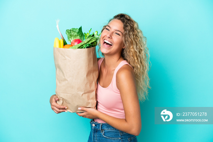 Girl with curly hair holding a grocery shopping bag isolated on green background laughing in lateral position