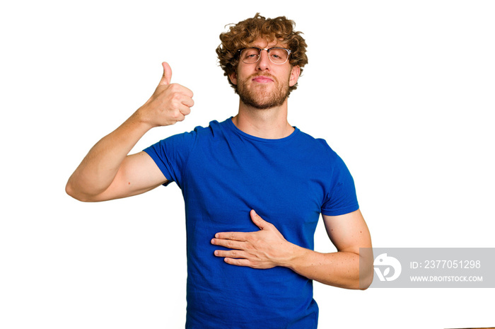 Young caucasian man isolated on green chroma background touches tummy, smiles gently, eating and satisfaction concept.