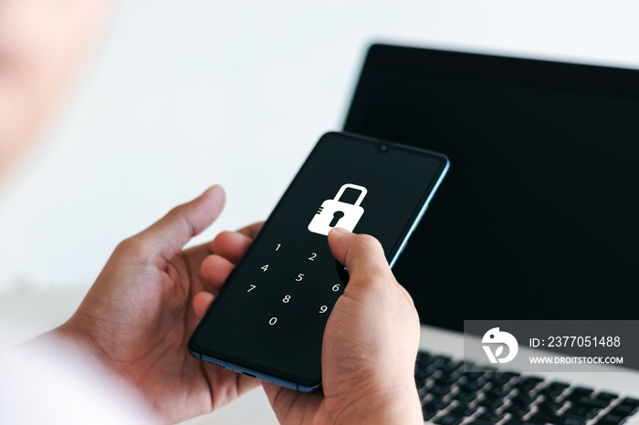 Hacking a Phishing mobile phone with a password to access a smartphone, security threats online, and fraud. A young man with a cell phone and laptop is secure in his bank account.