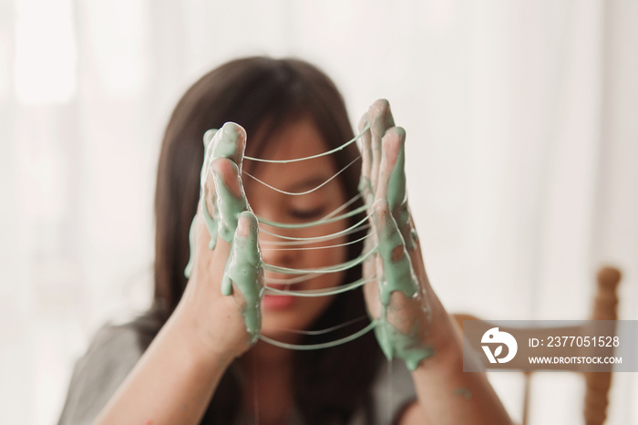 Hands with sticky slime, mixed Asian girl making homemade slime toy, sensory art and craft, fun homeschool chemistry project