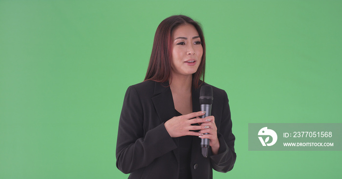 Asian millennial businesswoman speaking through microphone on green screen