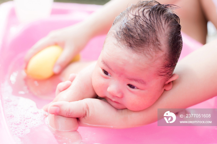 Asian newborn having a bath in ping basin by new mother