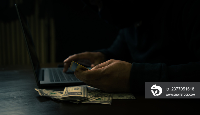 Hand of a man in a hoodie holding credit and using a laptop to hack credit card financial information - Internet theft concept