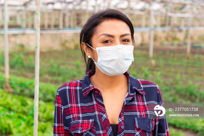 Hispanic woman gardener worker in protective face mask standing with rake at greenhouse farm