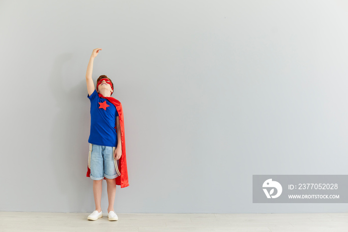 Smiling boy in costume of superhero standing and reaching up with hand