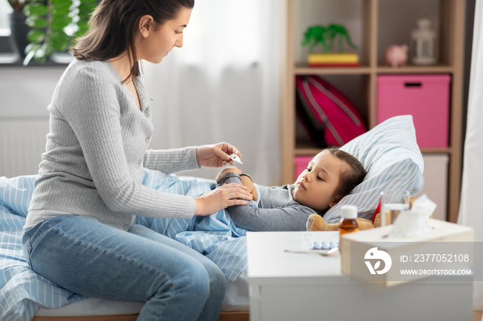 family, health and people concept - mother with thermometer measuring temperature of sick daughter lying in bed at home