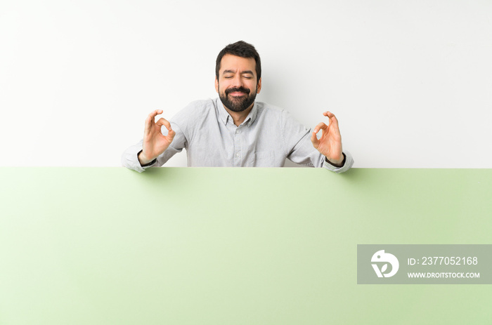 Young handsome man with beard holding a big green empty placard in zen pose