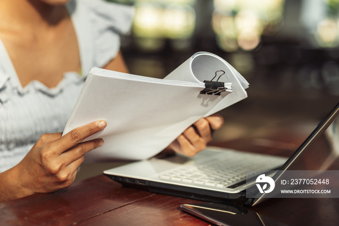 woman opening and reading a paper sheet near laptop on wooden table.