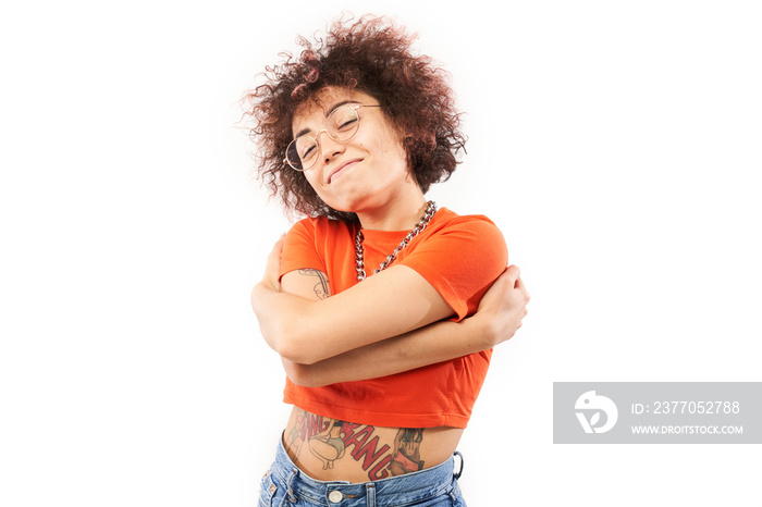 Young curly brunette woman hugging herself and smiling isolated on white studio background. Self love and self care concept.