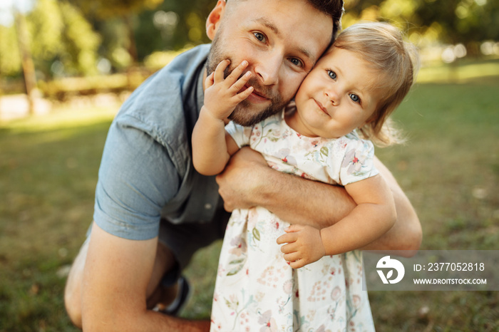 Portrait of young father with little daughter hugging at the park, spending weekends at the nature. Caring parent gently cuddle his lovely baby girl, enjoying joyful moments, concept of happy family