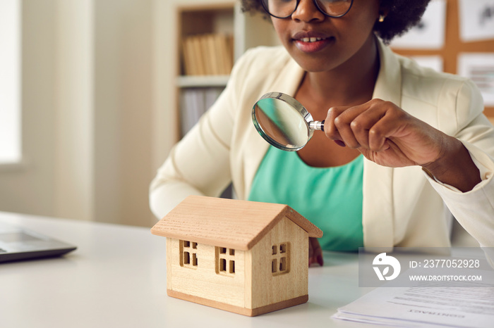 Real estate agent, lawyer or evaluator with magnifying glass looking at miniature house on her table. Find best apartment, buy or sell home, rent at good price, investigate property law case concept