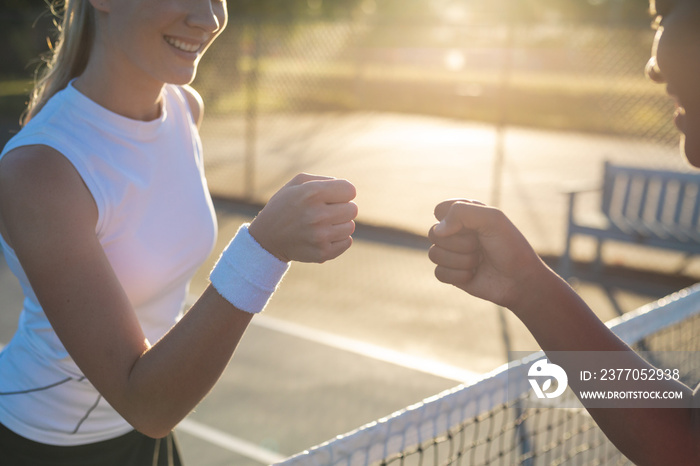 Smiling multiracial young female tennis players giving fist bump over net at court