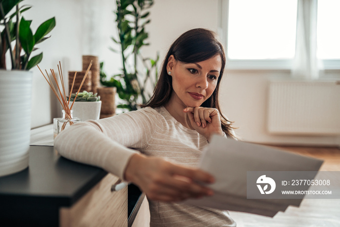 Pensive woman looking at received mail at home, holding blank envelopes.