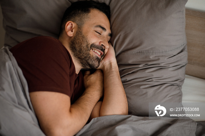 Happy man wakes up in the morning in a good mood in a gray bed