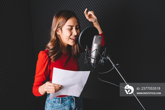 Pretty Asian female singer recording songs by using a studio microphone and pop shield on mic with passion in music recording studio. Performance and show in the music business. Image with copy space.