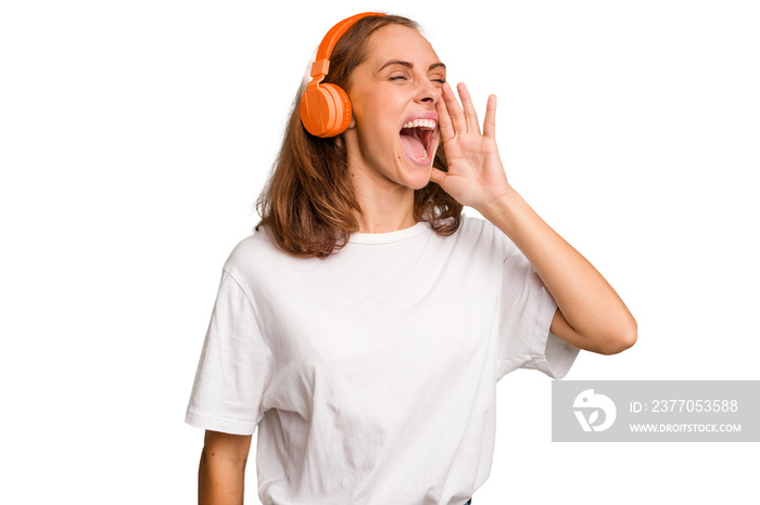 Young caucasian woman listening to music with headphones isolated shouting and holding palm near opened mouth.