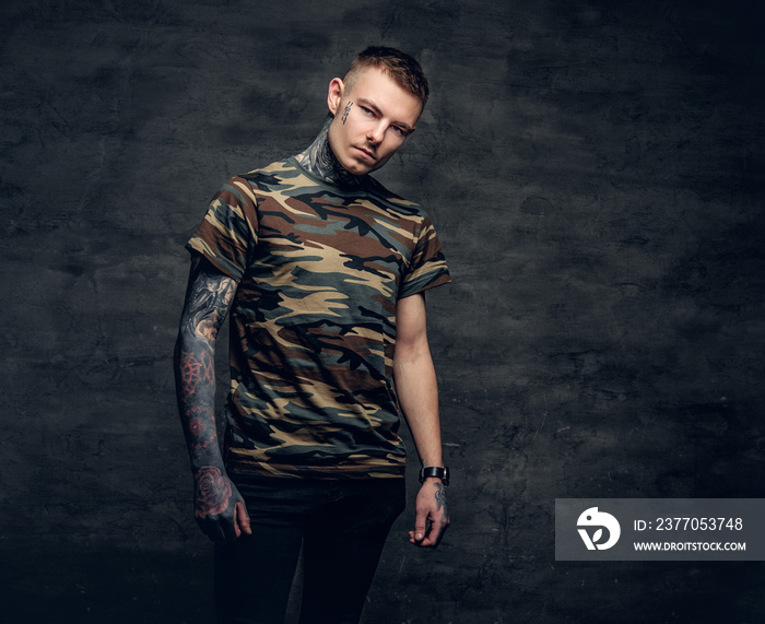 A man with tattoos on his neck, face and arms, dressed in a camouflage t shirt.