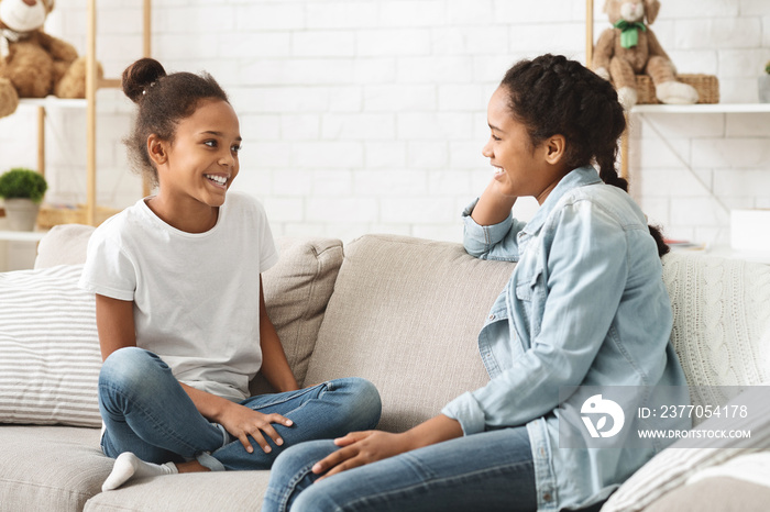 Two adorable girls sitting on sofa at home and talking