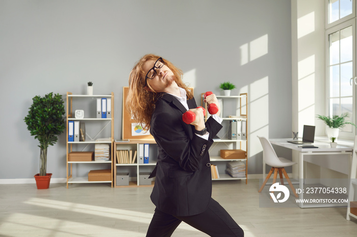 Sports workout at the office. Funny businessman or company employee leading hectic busy life but keeping fit anyway. Hilarious nerdy worker in glasses doing exercise with dumbbells during working day