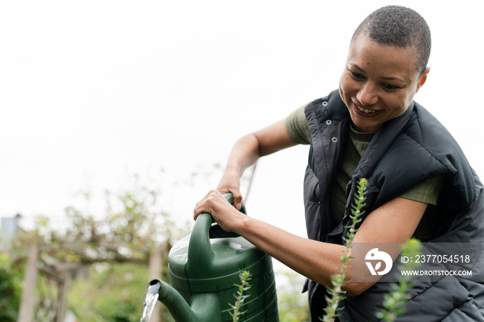 Smiling woman watering homegrown vegetables in urban garden