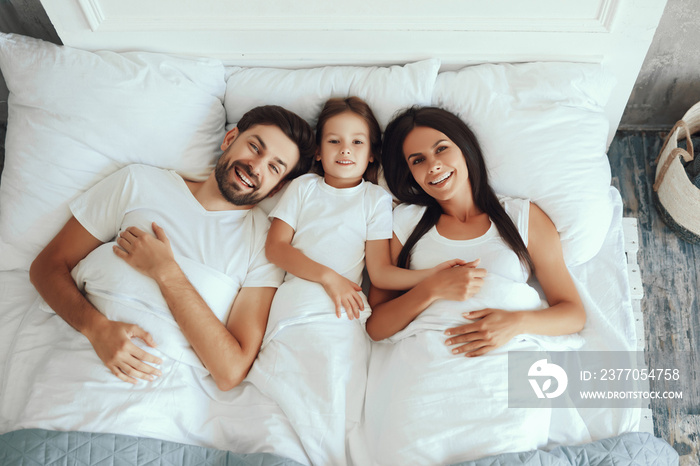 Joyous father enjoying morning in bed with wife and daughter