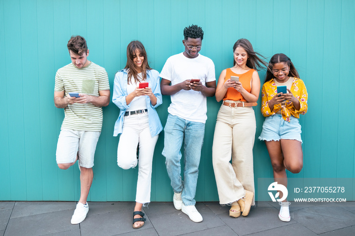 Group multiracial friends using smartphones outside. Group of fashion friends watching on their smart mobile phones. Millennial generation z addicted to new technology trends.