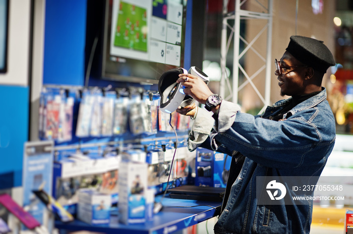 Stylish casual african american man at jeans jacket and black beret using vr glasses at electronics store.