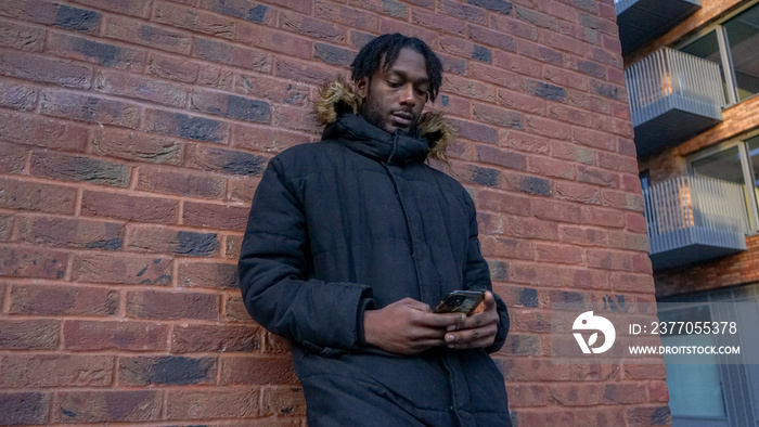 Young man leaning against brick wall, looking at smart phone