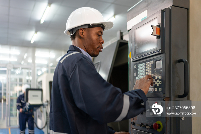 Male engineer operating cnc machine in control panel at factory. Man technician in uniform and helmet safety working at workshop heavy metal industrial